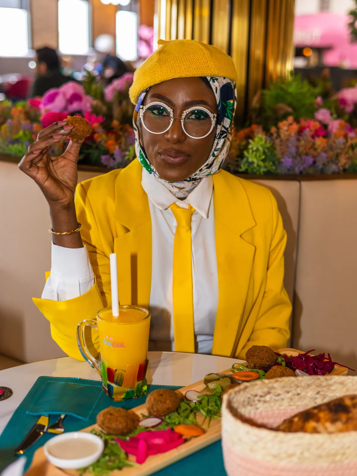 Azeezat at a restaurant table holding up a falafel